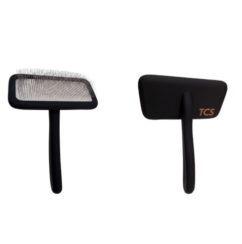 Two black pet grooming brushes shown side by side on a plain white background, one displaying the bristle head and the other showing the handle with a small gold TCS logo.