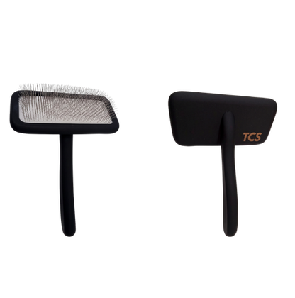 Two black pet grooming brushes shown side by side on a plain white background, one displaying the bristle head and the other showing the handle with a small gold TCS logo.